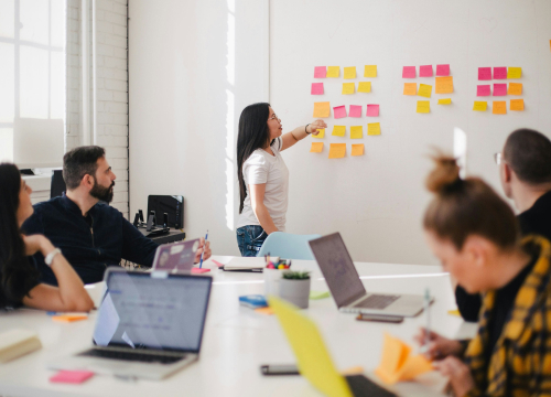 Mulher fixando post-it com equipe observando