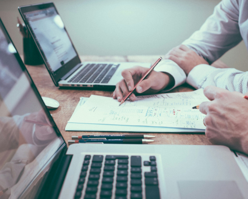 Pessoas realizando anotações no papel com notebook na mesa